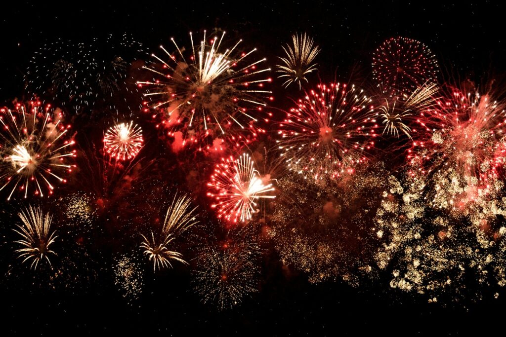Red, yellow, and white fireworks explode in the nighttime sky.