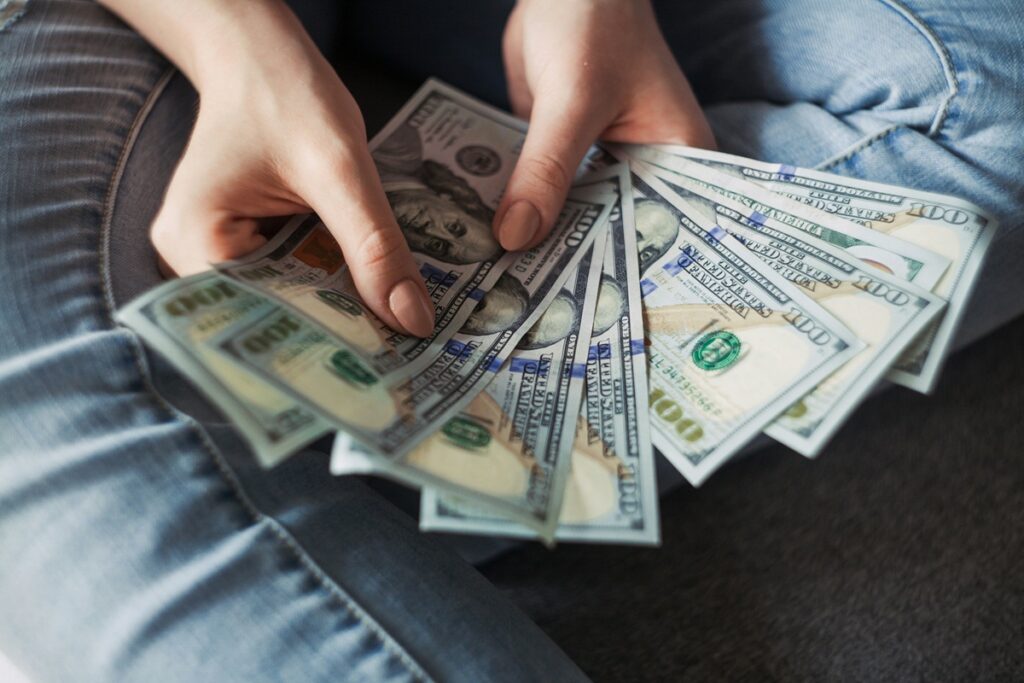 Two hands, with painted nails, hold nine one-hundred dollar bills.