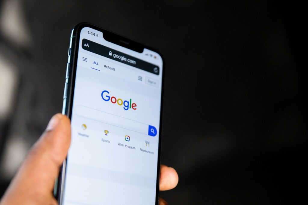 A hand holds a cell phone opened to the Google searched page.