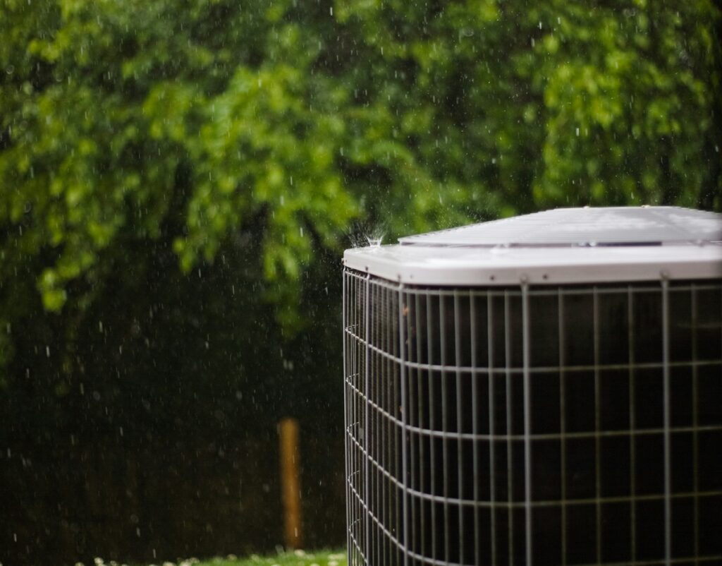 An air conditioner sits in front of trees.