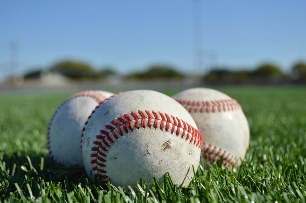 Three baseballs sit on a patch of grass.
