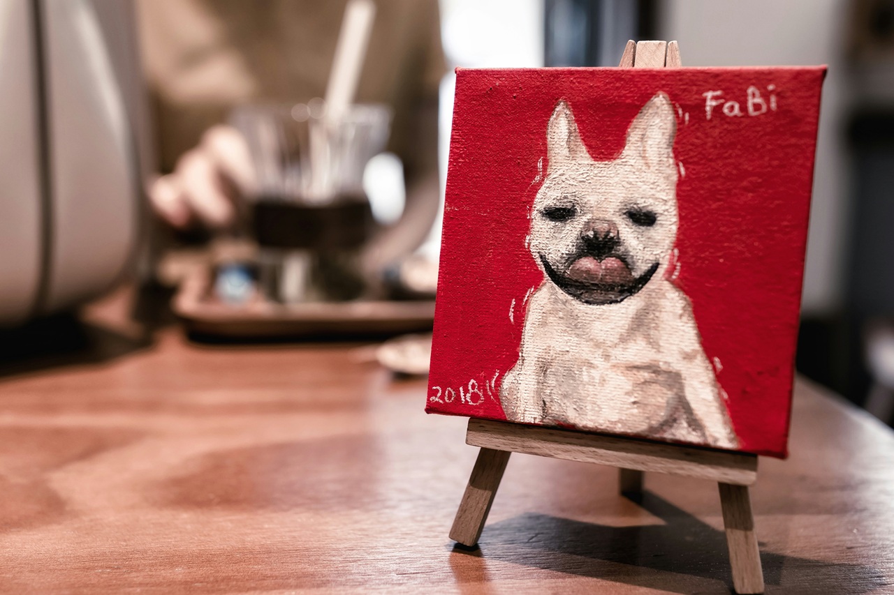 A painting of a brownie dog that says Fabi on the top and 2018 on the bottom. The painting is sitting on a table.