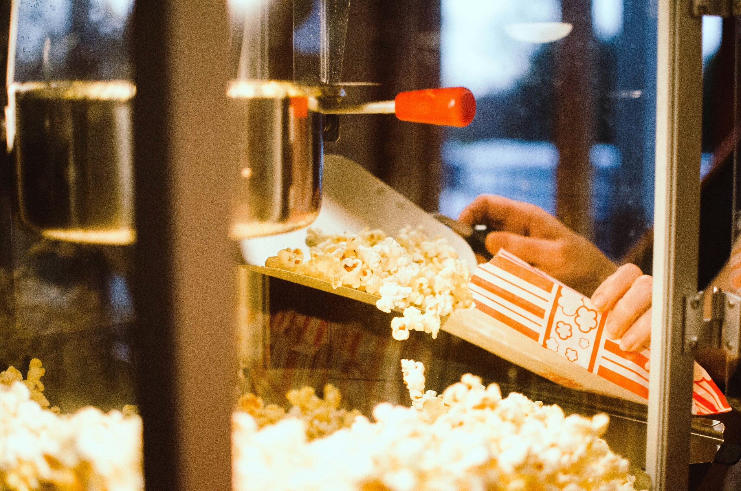 A hand putting popcorn into a popcorn box, using a silver metal scooper.