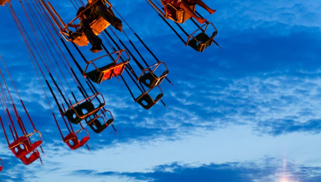 Flying swings, with legs dangling down, at an amusement park against the backdrop of a darkening sky.