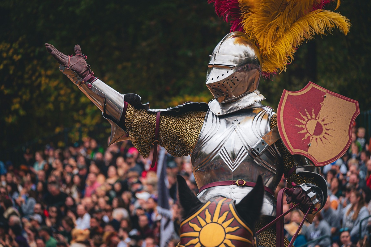 A knight in shining armor holds his hand up as he holds a red and gold shield.