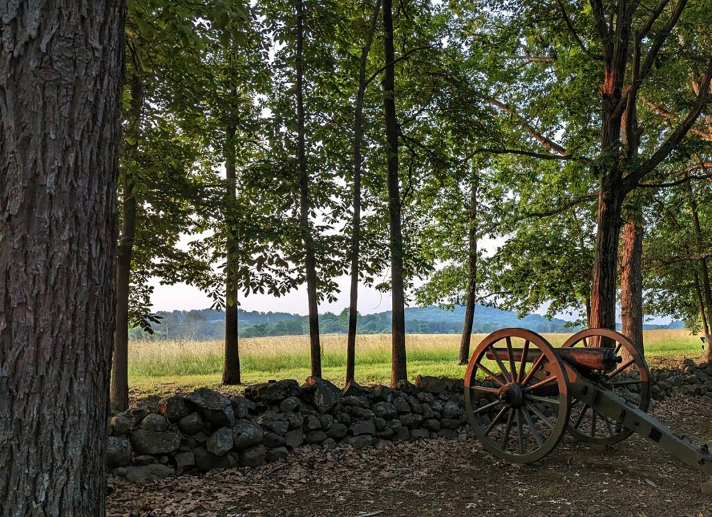 A cannon sits among trees, in front of a rock wall, at Gettysburg National Military Park.