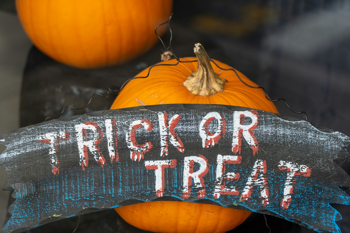 A black sign that says "Trick or Treat' sits against pumpkins.